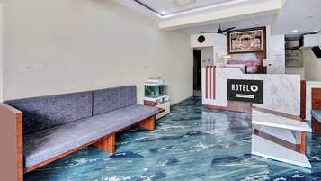 A hotel reception area with a marble floor, a sofa, a reception desk, and a clock on the wall.