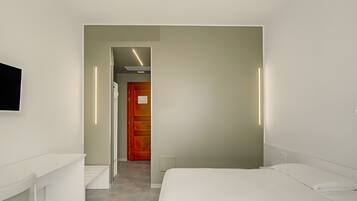 A modern hotel room with a bed, a desk, and a television on the wall.