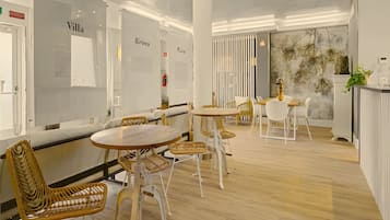 A modern interior with round tables and wicker chairs, white walls, and a wooden floor.