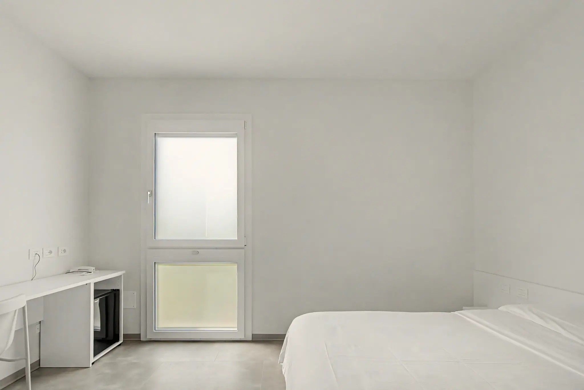 A minimalist bedroom with a single bed, a desk, and a window.