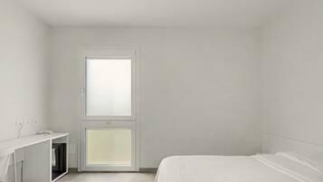 A minimalist bedroom with a single bed, a desk, and a window.