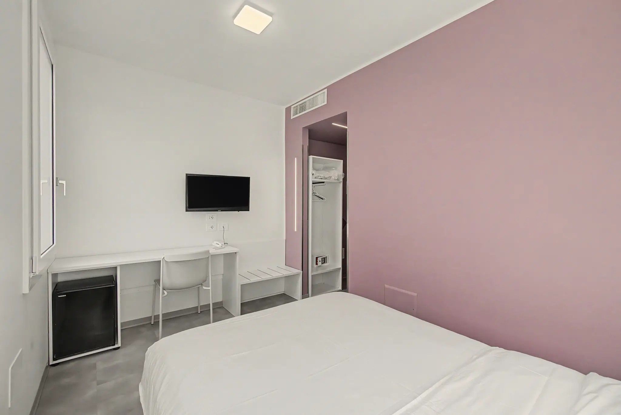 Ein Hotelzimmer mit einem Bett, einem Schreibtisch mit Stuhl, einem Fernseher und einem begehbaren Kleiderschrank.