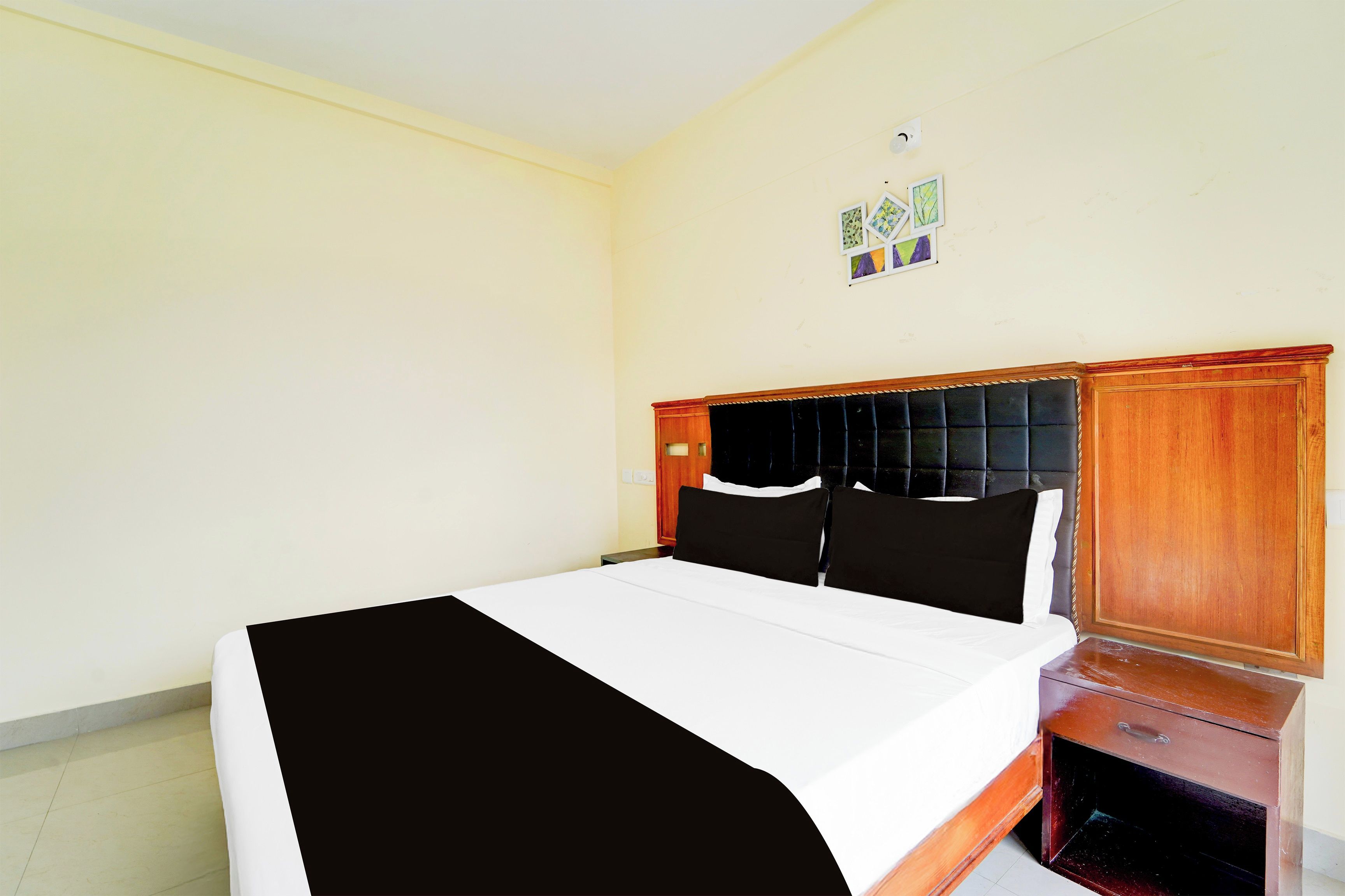 Habitación de hotel con una cama, una mesita de noche, un armario de madera y una lámpara fijada a la pared.
