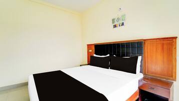 Habitación de hotel con una cama, una mesita de noche, un armario de madera y una lámpara fijada a la pared.