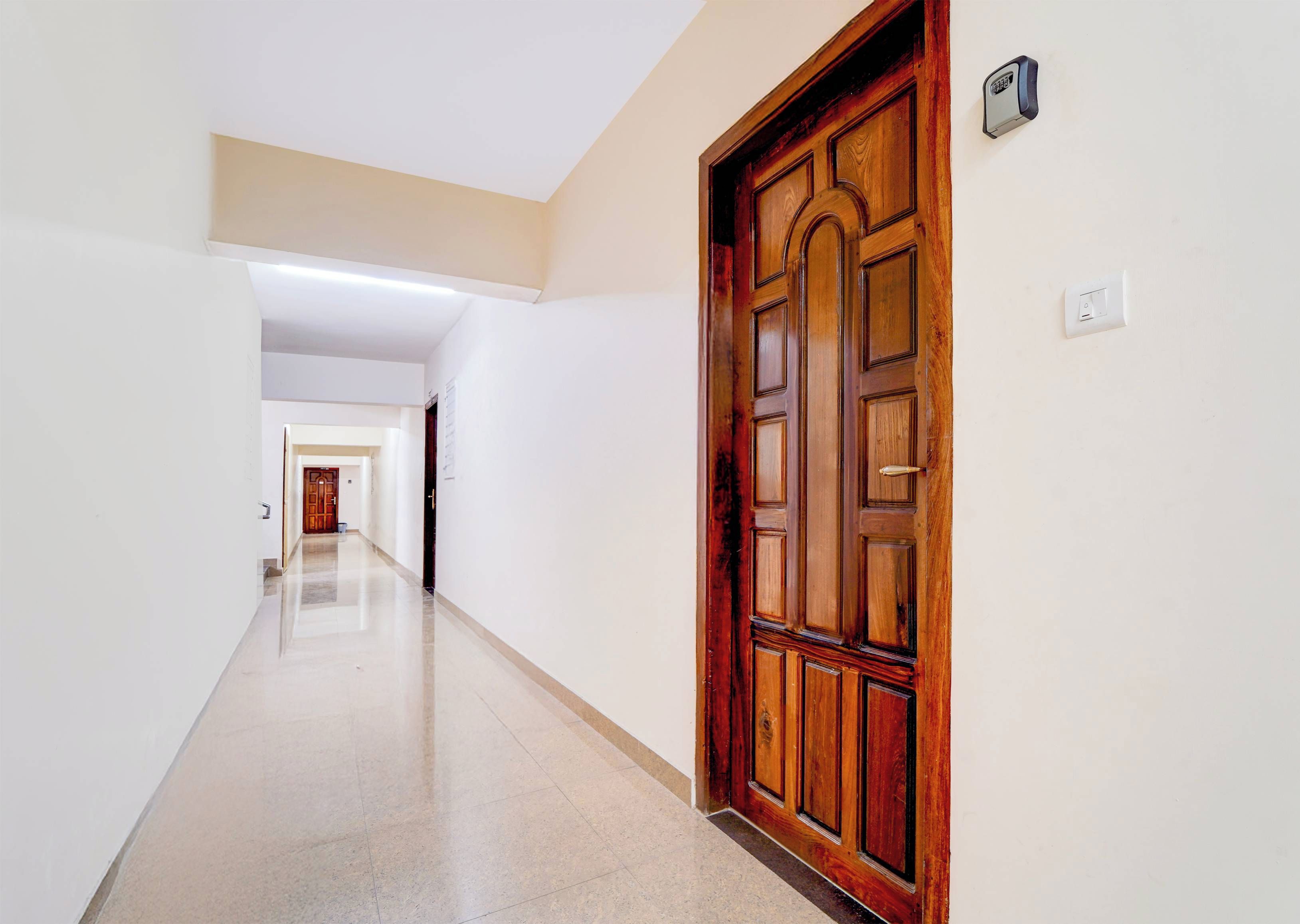 A corridor with a wooden door on the right, a light switch, and a security device on the wall.