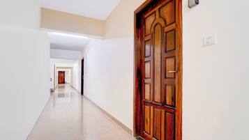 A corridor with a wooden door on the right, a light switch, and a security device on the wall.