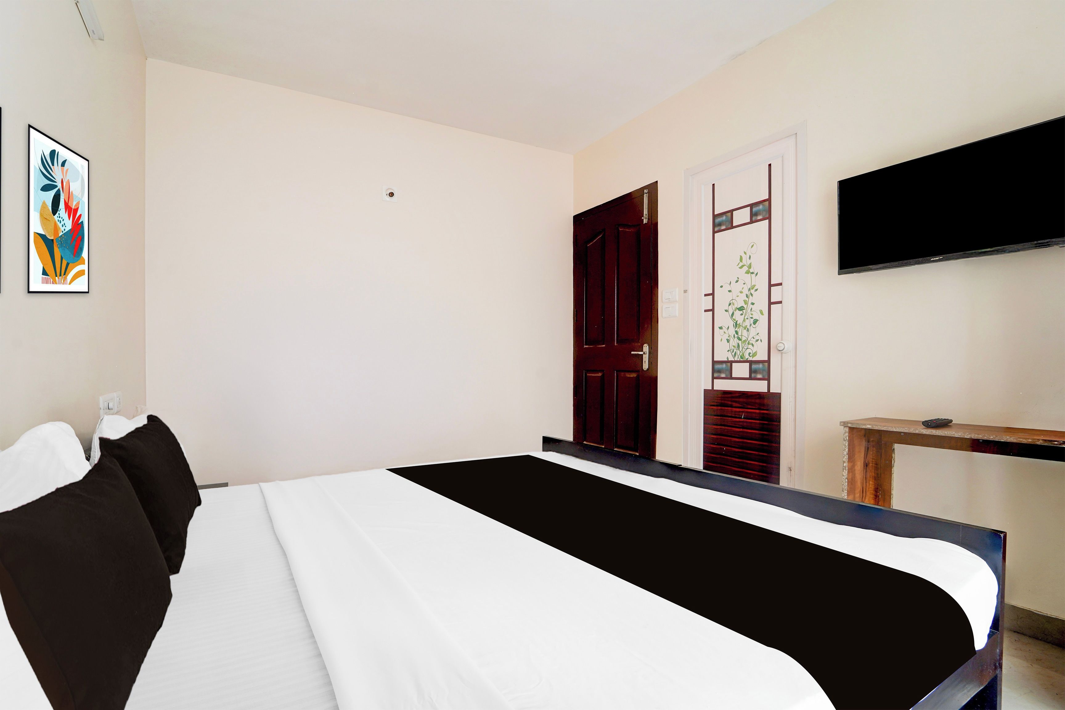 Quarto de hotel com cama, televisão, porta e quadro fixado na parede.