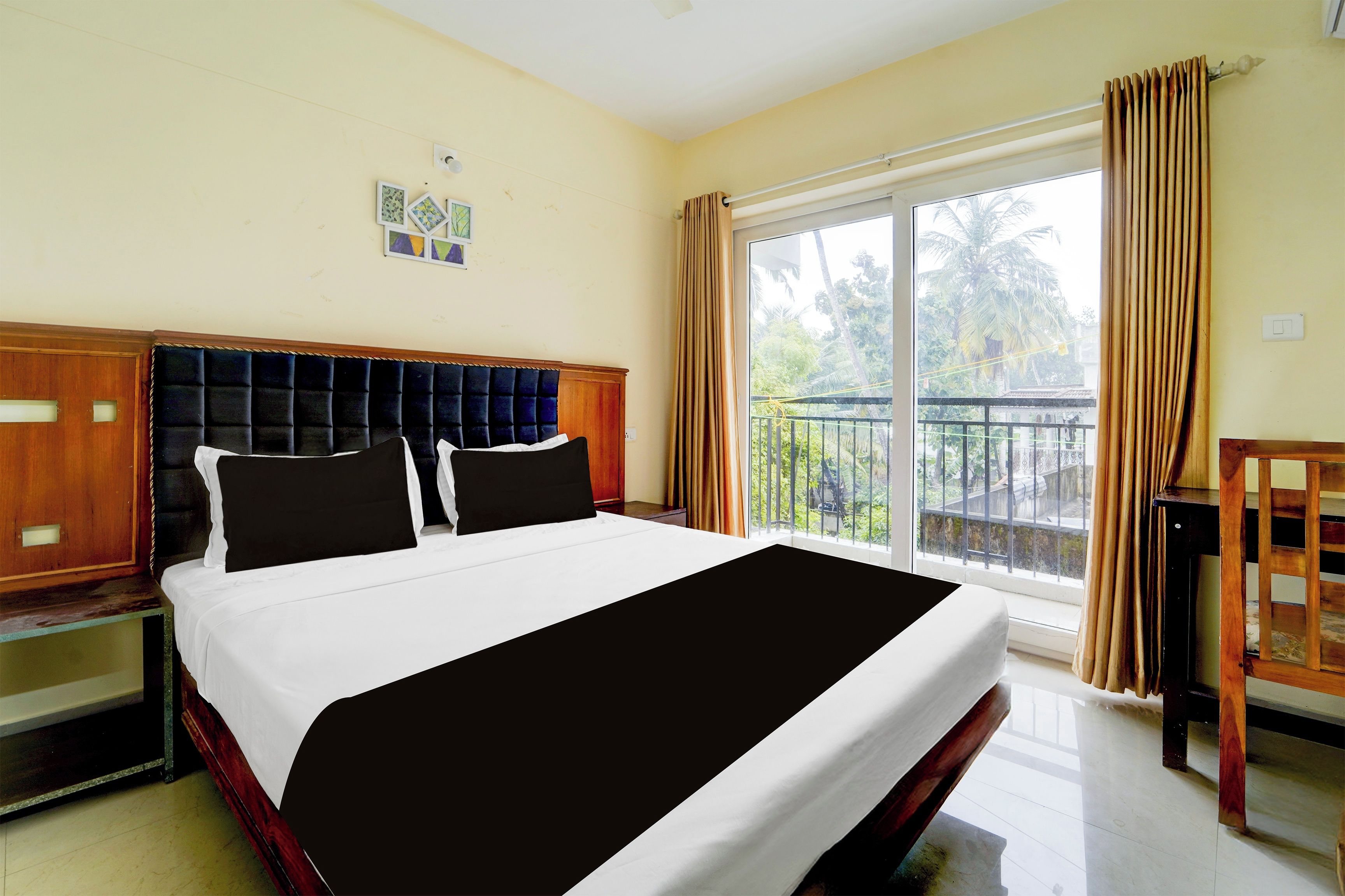 Habitación de hotel con una cama grande, cabecera de madera, balcón con vista a palmeras y ventana con cortinas.