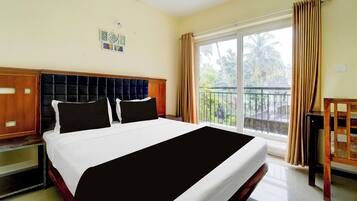 Habitación de hotel con una cama grande, cabecera de madera, balcón con vista a palmeras y ventana con cortinas.