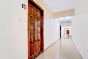 Corredor com porta de madeira, interruptor de luz e chão limpo revestido de azulejos.