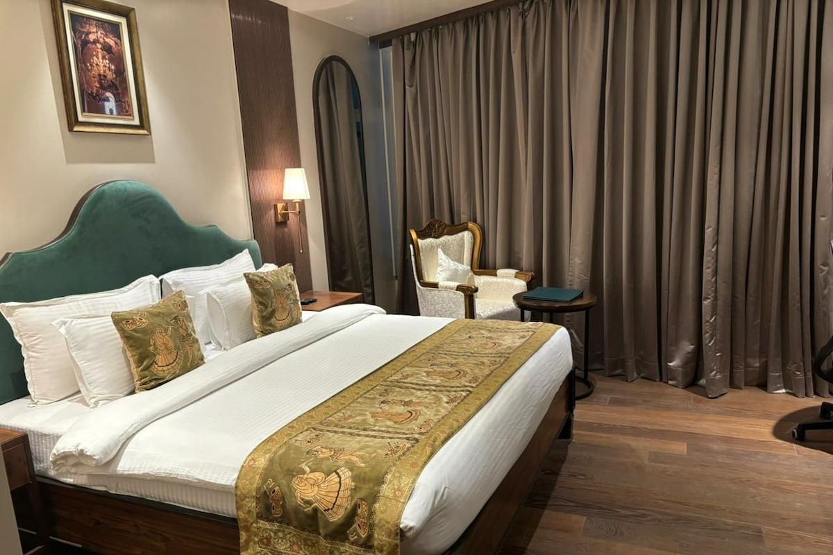 Una habitación de hotel con una cama grande, una silla, una mesita y una cortina.
