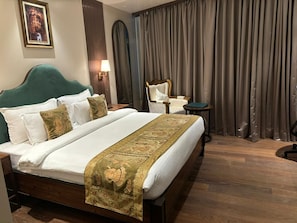 A hotel room with a large bed, a chair, a small table, and a curtain. - The Mantis Hotels & Resorts (Muzaffarpur)