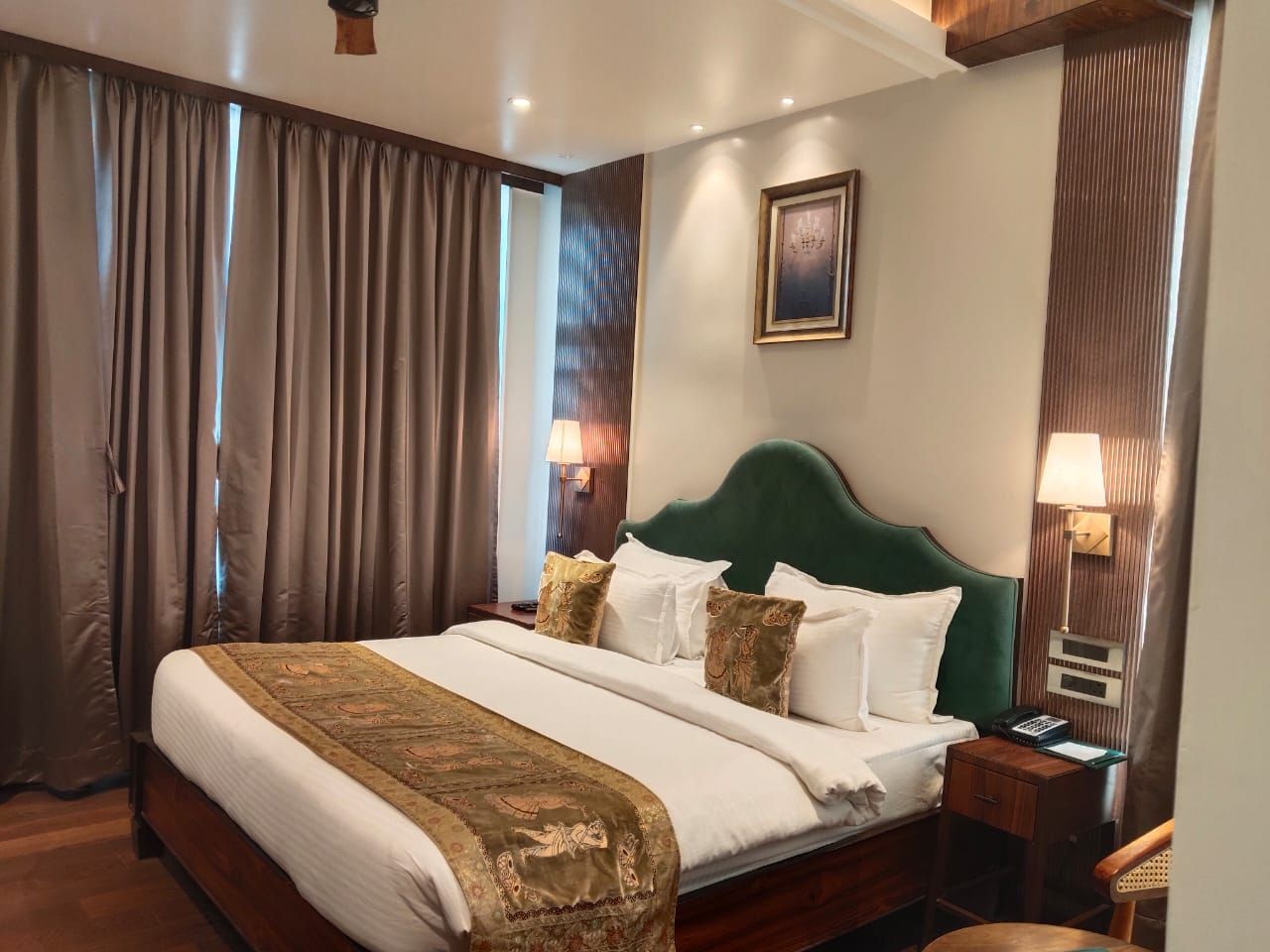 A hotel room with a large bed, a wooden headboard, two bedside tables with lamps, and a framed picture on the wall.