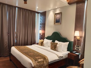 Habitación de hotel con una cama grande, cabecera de madera, dos mesitas de noche con lámparas y un cuadro enmarcado en la pared.