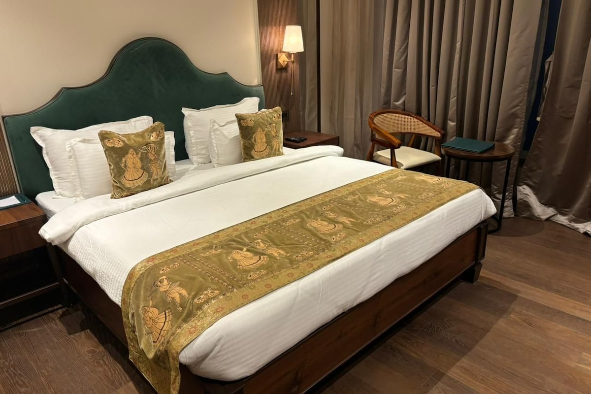 Una habitación de hotel con una cama grande, una mesita de noche, una silla y una lámpara.