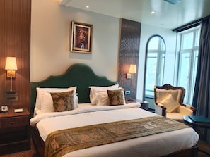 Habitación de hotel con una cama grande, dos lámparas de noche, un cabecero, una ventana con cortinas y un cuadro en la pared.