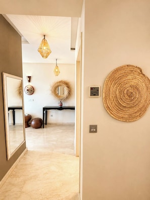 Un couloir avec un miroir, une œuvre d’art murale tissée et une console sur laquelle est posé un vase.