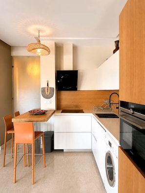 Une cuisine compacte avec un coin repas, un lave-linge et un téléviseur fixé au mur.