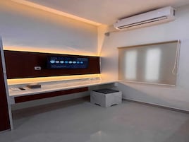 Un baño moderno con televisión integrada, un taburete pequeño y una ventana.