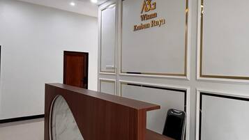 A reception desk with a marble top, a wooden counter, and a black chair. The wall behind has a sign with gold lettering.