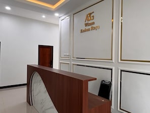 A reception desk with a marble top, a wooden counter, and a black chair. The wall behind has a sign with gold lettering. - Cozzy Wisma Embun Raya A3G (PALANGKA RAYA)