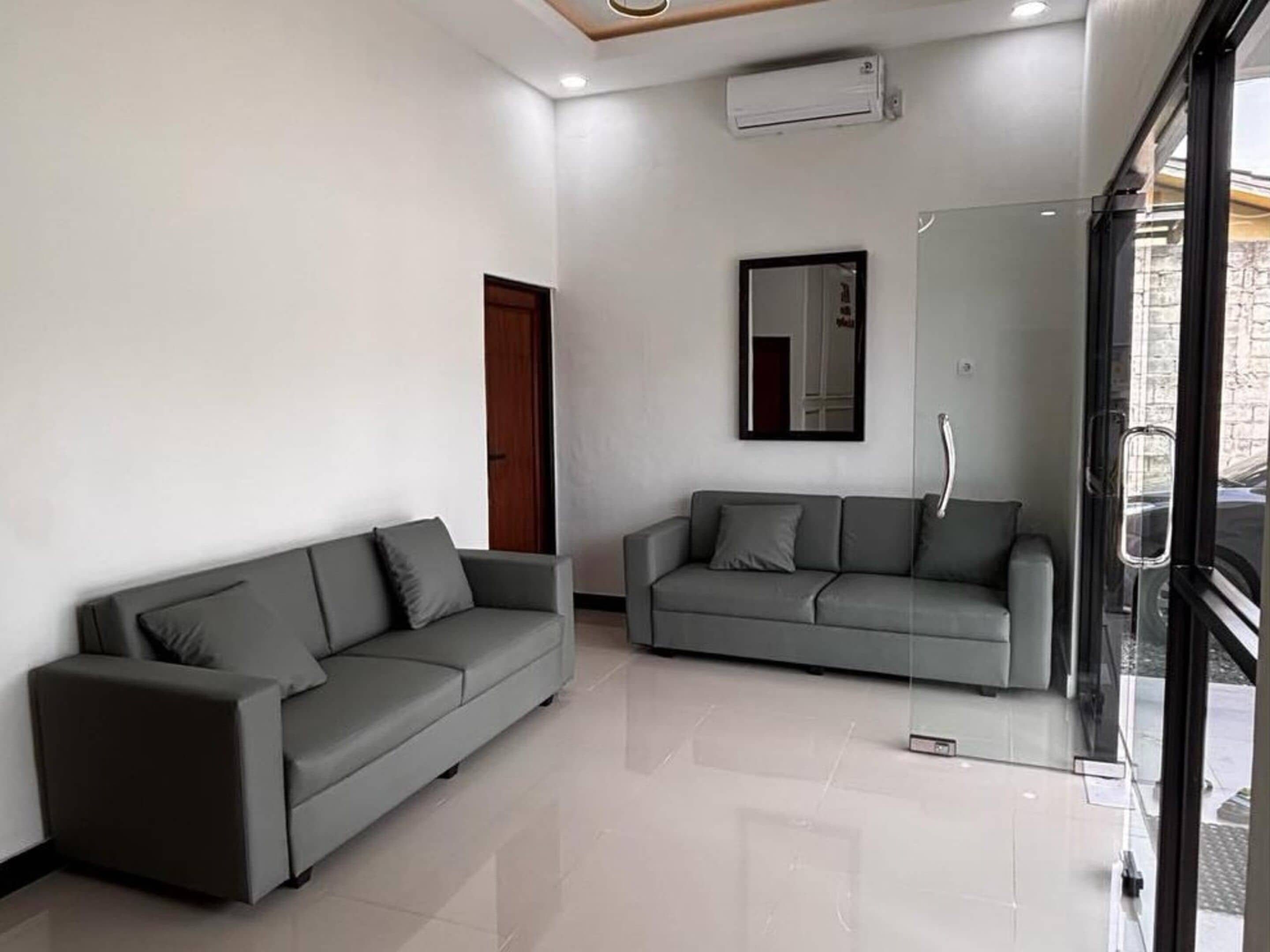 A modern living room with two grey sofas, a large mirror, and a glass door leading outside.