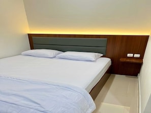 A hotel room with a bed, two pillows, a nightstand with a lamp, and a wooden headboard. - Cozzy Wisma Embun Raya A3G (PALANGKA RAYA)