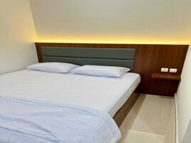 Una habitación de hotel con cama, dos almohadas, mesita de noche con lámpara y cabecero de madera.