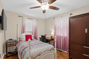 A bedroom with a bed, a desk, a wardrobe, a ceiling fan, and a television mounted on the wall. - Paws & Relax | Fredericksburg Home with Fire Pit (Fredericksburg)