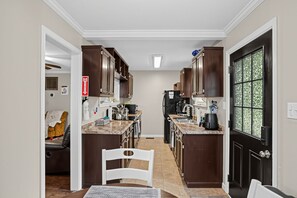 A kitchen with dark wooden cabinets, a marble countertop, and a black refrigerator. - Paws & Relax | Fredericksburg Home with Fire Pit (Fredericksburg)