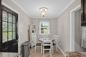 A compact kitchen with a dining table, chairs, a trash bin, and a window with blinds. - Paws & Relax | Fredericksburg Home with Fire Pit (Fredericksburg)