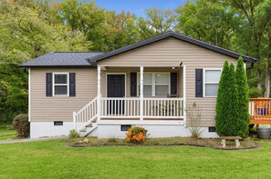 A single-story house with a front porch, a small garden, and a tall coniferous tree. - Paws & Relax | Fredericksburg Home with Fire Pit (Fredericksburg)