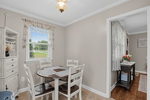 A dining area with a round table, white chairs, and a window with curtains. - Paws & Relax | Fredericksburg Home with Fire Pit (Fredericksburg)