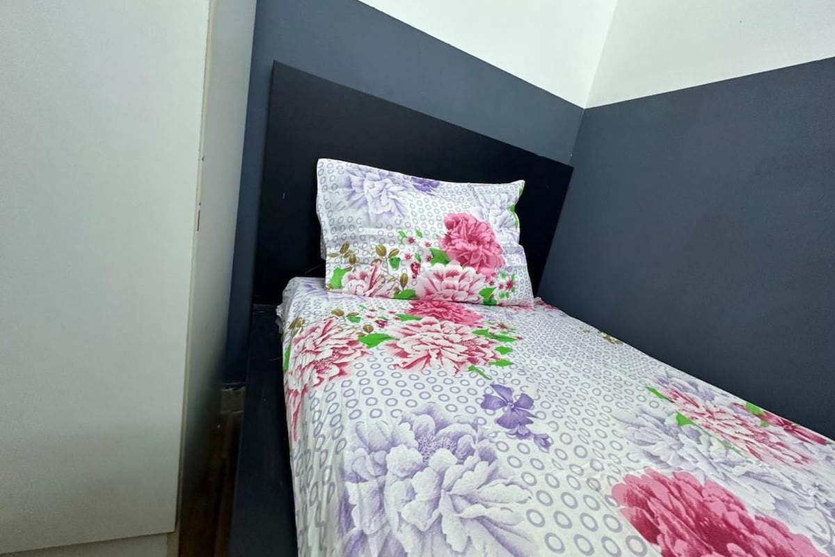 Een bed met een bloemenprint sprei en een donker hoofdbord in een kamer met een witte deur en donkere muren.