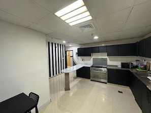 A kitchen with a stove, microwave, and a dining area with a table and chairs. - Euphoria Partition Room in Al Barsha1 (Dubai)