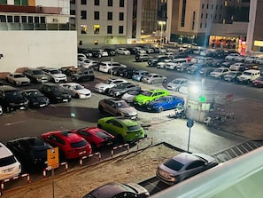 A parking lot with multiple cars, a sign indicating a parking area, and a building with illuminated windows in the background. - Euphoria Partition Room in Al Barsha1 (Dubai)