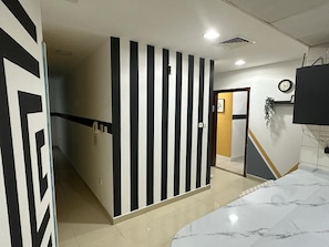 A hotel room with a curved marble bed, a striped wall, a door leading to another room, and a clock on the wall. - Euphoria Partition Room in Al Barsha1 (Dubai)