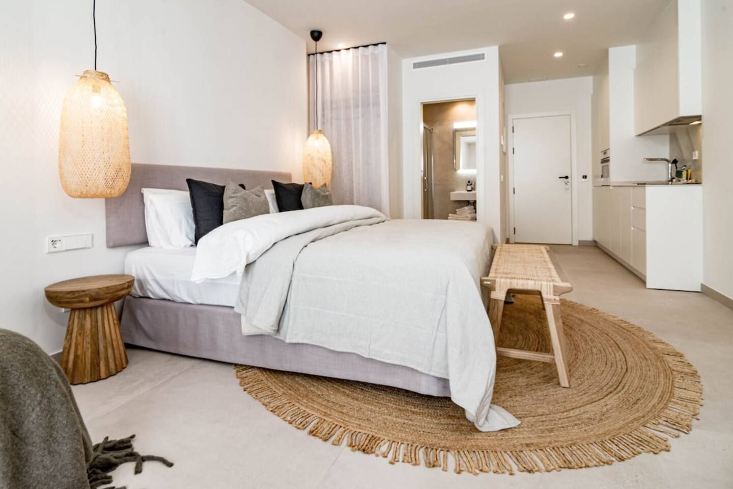 Een moderne slaapkamer met een bed, nachtkastjes, een bedlampje, een houten bankje en een rond vloerkleed.