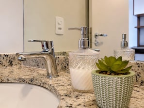 Une salle de bain dotée d’un comptoir en granit, d’un robinet en acier inoxydable, d’un distributeur de savon en verre transparent et d’une plante succulente en pot.