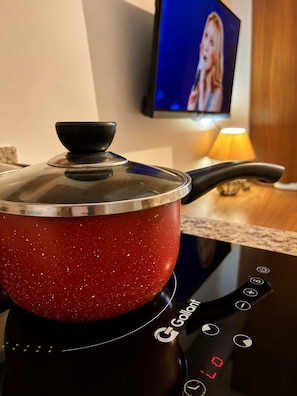 A red pot on an induction cooktop with a logo, a television in the background, and a lamp on the counter. - SETIN 1504 (São Paulo)