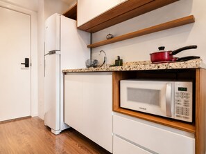 A compact kitchen with a white refrigerator, a microwave, and a wooden shelf above the countertop. - SETIN 1504 (São Paulo)