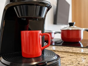 Une cafetière posée sur la plaque de cuisson, avec une tasse rouge à côté.