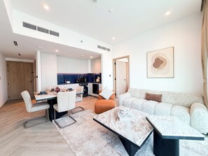A modern living room with a sofa, coffee table, and dining area. - Beautiful 2BR apartment in Peninsula Three, Breathtaking Canal view (Dubai)