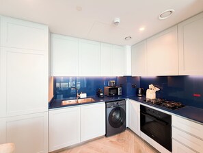 A modern kitchen with white cabinetry, a built-in washing machine, a microwave, a coffee maker, and a gas stove. - Beautiful 2BR apartment in Peninsula Three, Breathtaking Canal view (Dubai)