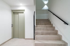 Una escalera con barandilla, una puerta con interruptor de luz y una lámpara en el techo.