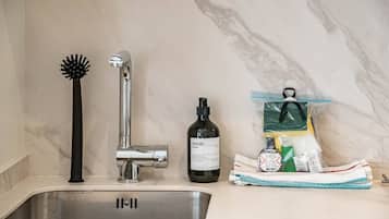 A bathroom sink with a chrome faucet, a black hairbrush, a bottle of Meraki, and a towel with cleaning supplies.
