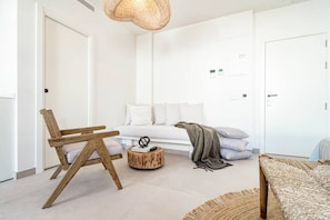 Una habitación minimalista con una silla de madera, una mesa redonda de madera, un sofá blanco y una alfombra estampada.