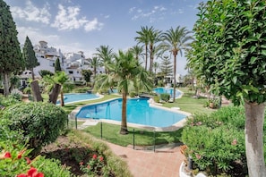A pool area with multiple swimming pools, surrounded by lush greenery and palm trees. - AB3 - Spacious holiday home, Puerto Banus (Marbella)