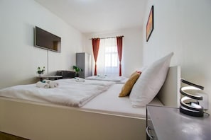 Een hotelkamer met een bed, een bureau, een televisie, een raam met gordijnen en een nachtkastje met een lamp.
