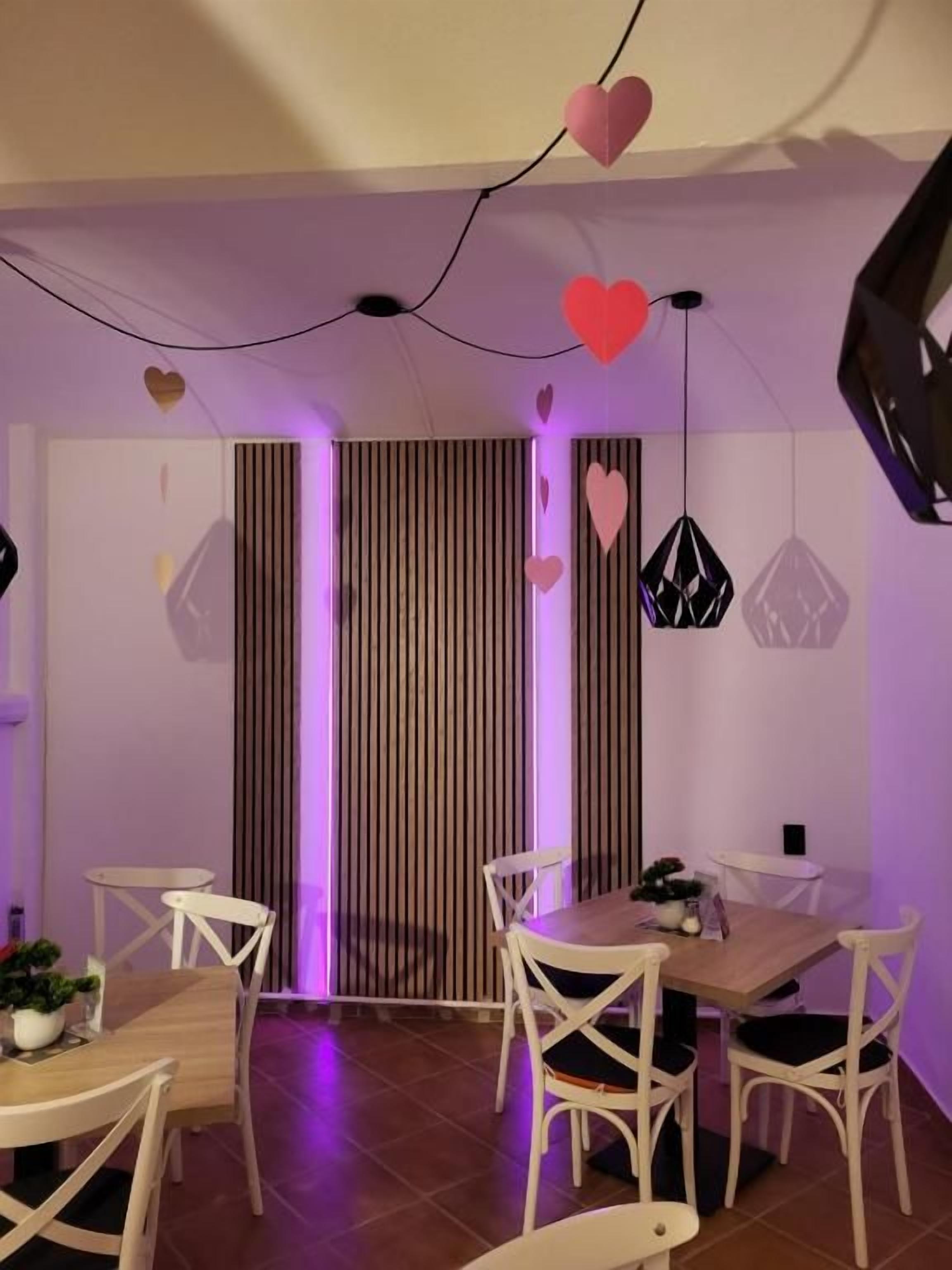 Un coin repas avec une table en bois et des chaises blanches, un mur à rayures et des décorations en forme de cœur suspendues.